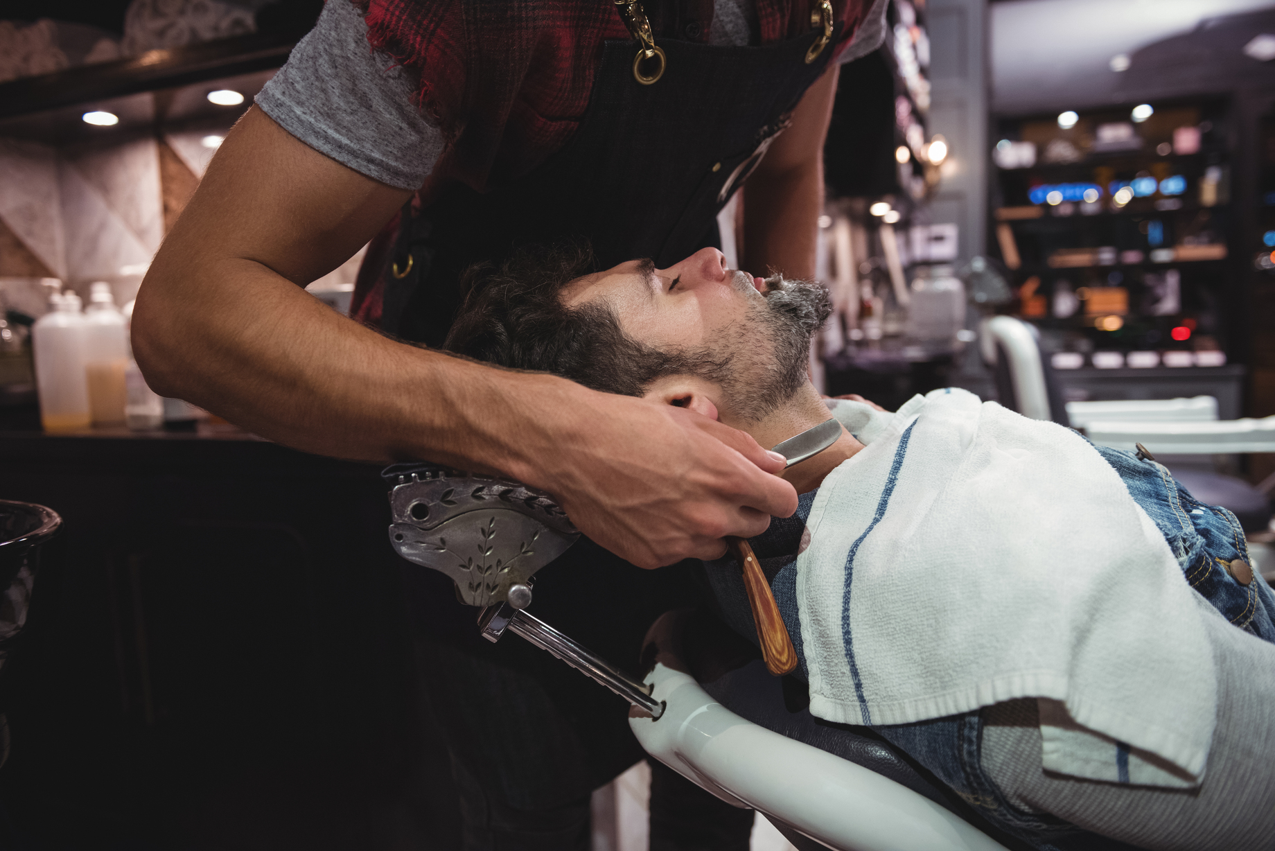 Man getting his beard shaved with razor in barber shop